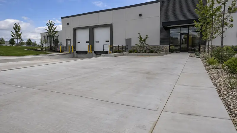 Concrete commercial entrance leading to a low-rise light industrial business with separated sidewalk and service access.